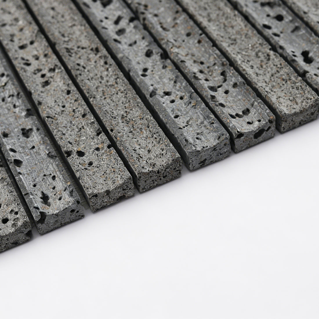 Edge close-up of dark grey lava stone linear mosaic.