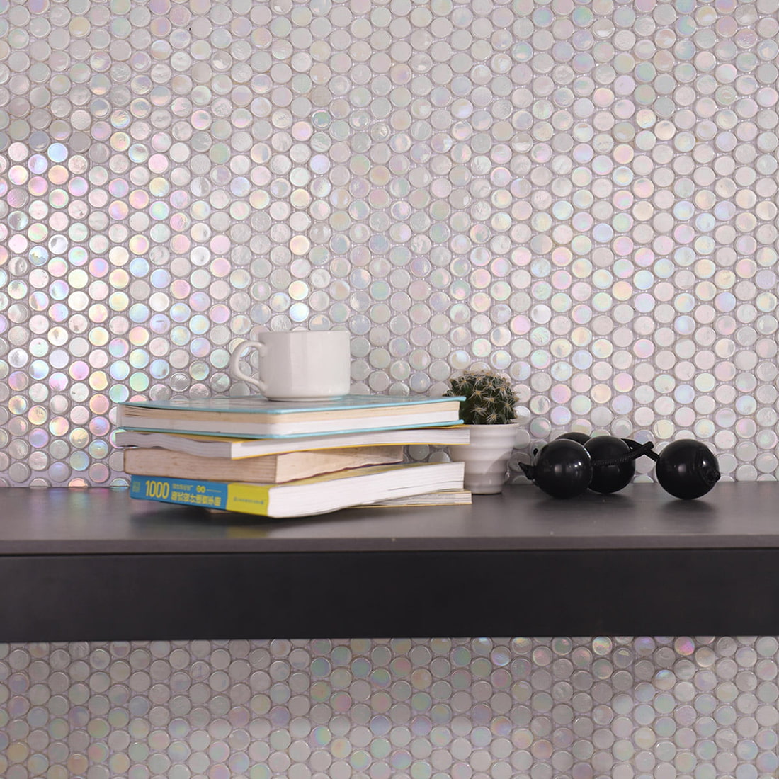 A wall covered in iridescent penny tiles behind a shelf with books and a coffee cup.
