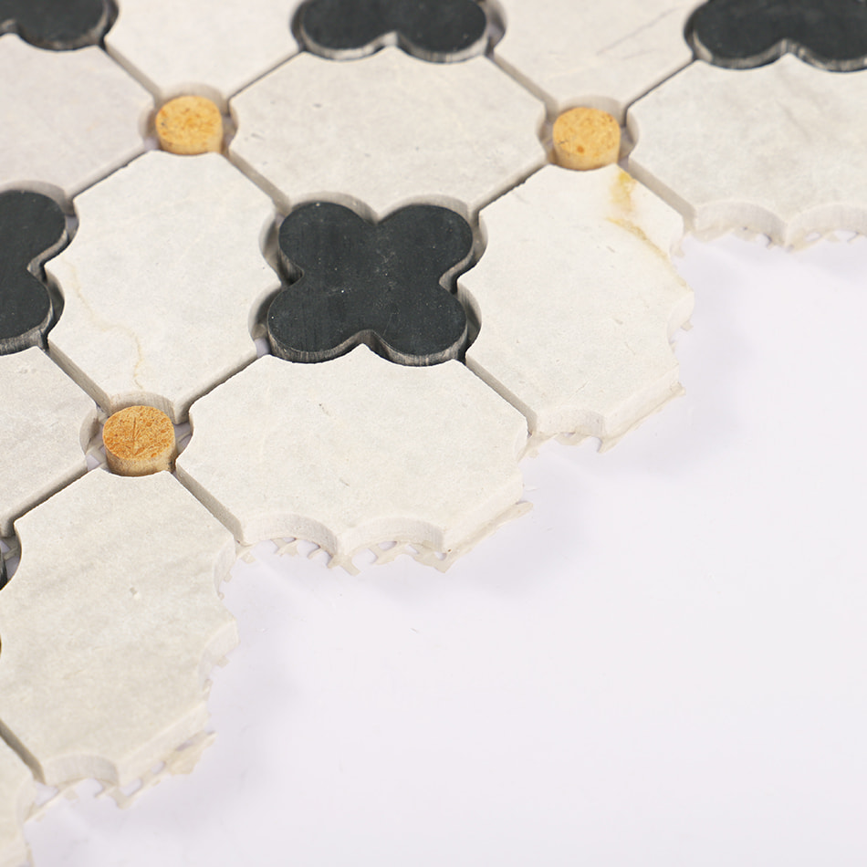 Edge close up of light gray marble tile with black quatrefoil and yellow dots