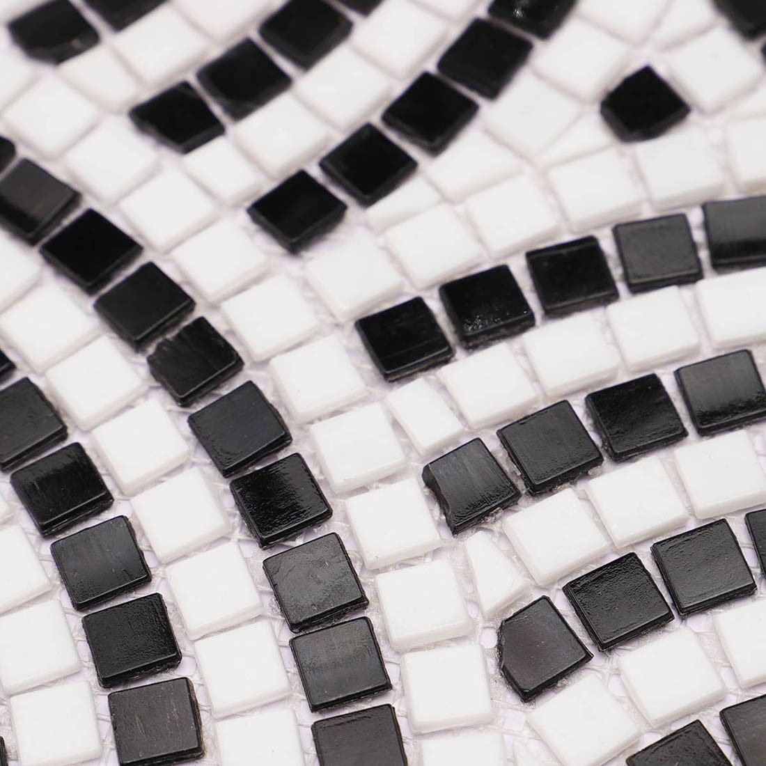 Macro close-up of handmade black and white fan pattern glass mosaic tile showing glossy texture and fine craftsmanship