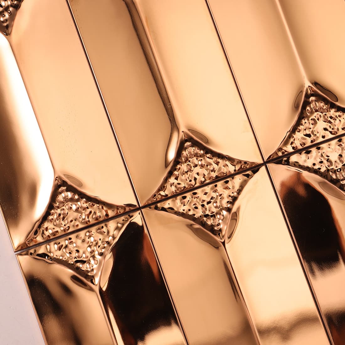 Extreme close-up of the pebbled hammered texture on rose gold metal tiles.