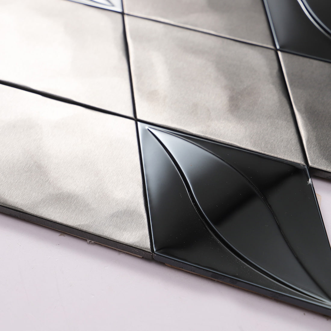 Angled edge view showing the raised 3D design on the mirror black stainless steel tile.