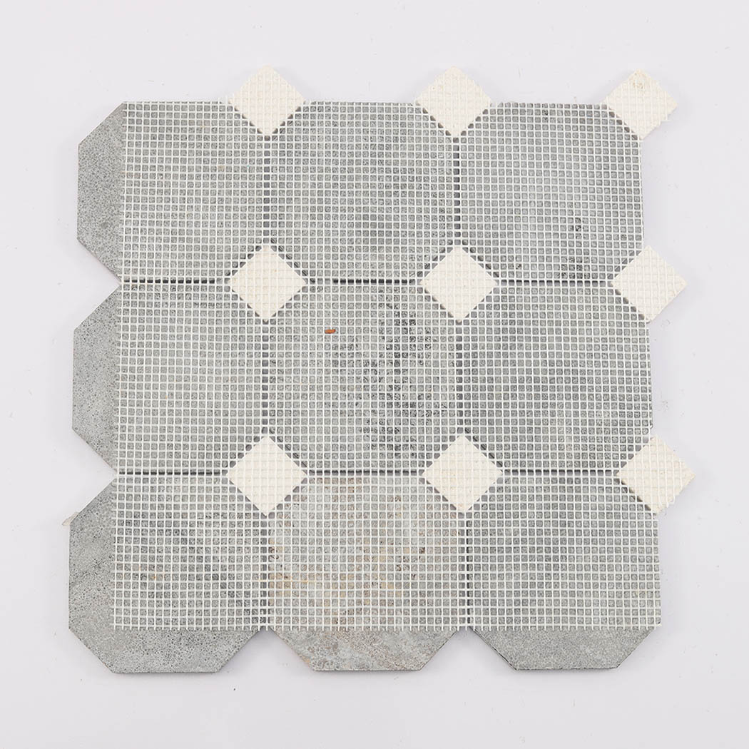 The back view of an interlocking stone mosaic tile showing the fiber mesh grid.
