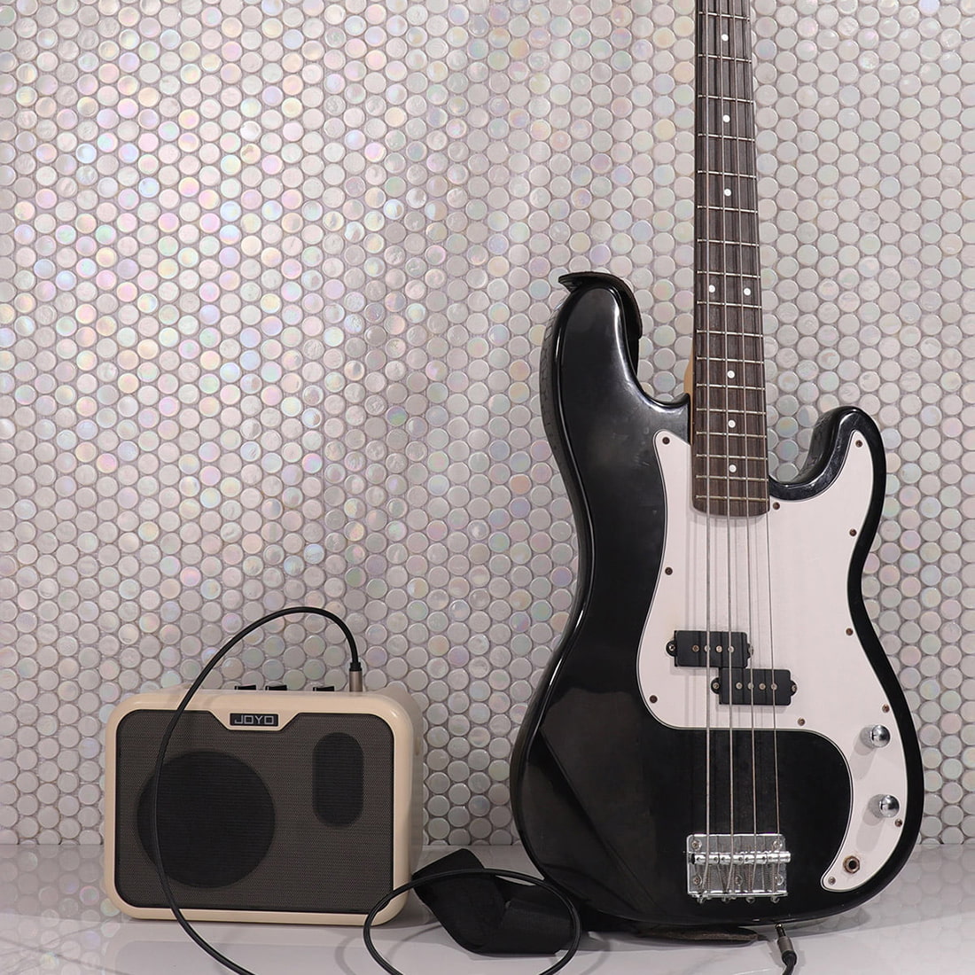 A shimmering white iridescent penny tile wall acting as a backdrop for a guitar and amplifier.