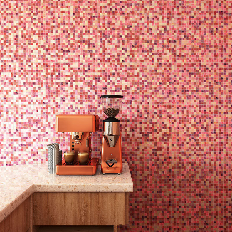 Pink glass square tile backsplash behind a copper espresso machine and terrazzo counter.