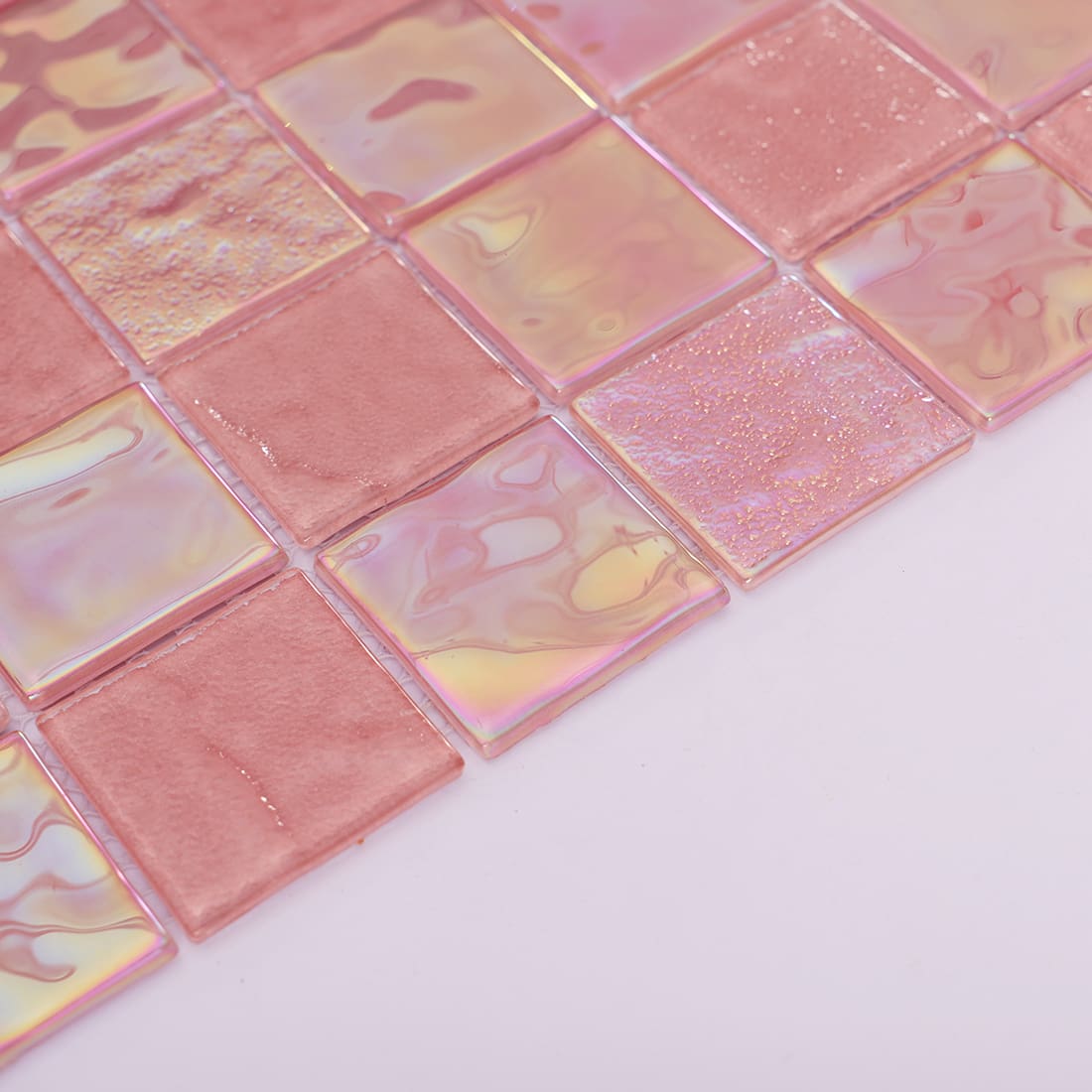 Angled view of pink square glass mosaic tile sheet with iridescent glossy surface