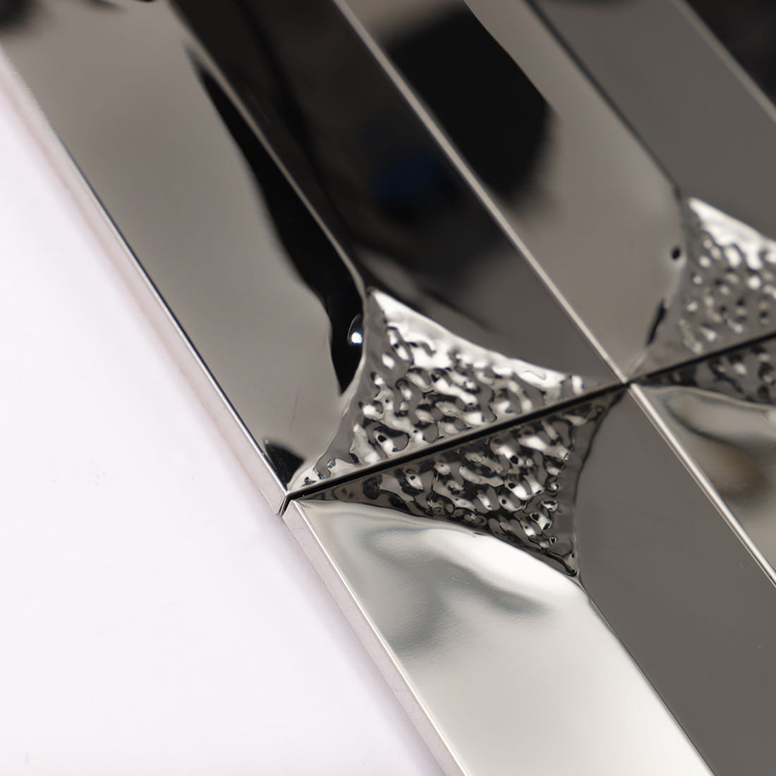 Detailed view of the beveled edges on silver reflective metal mosaic tiles.