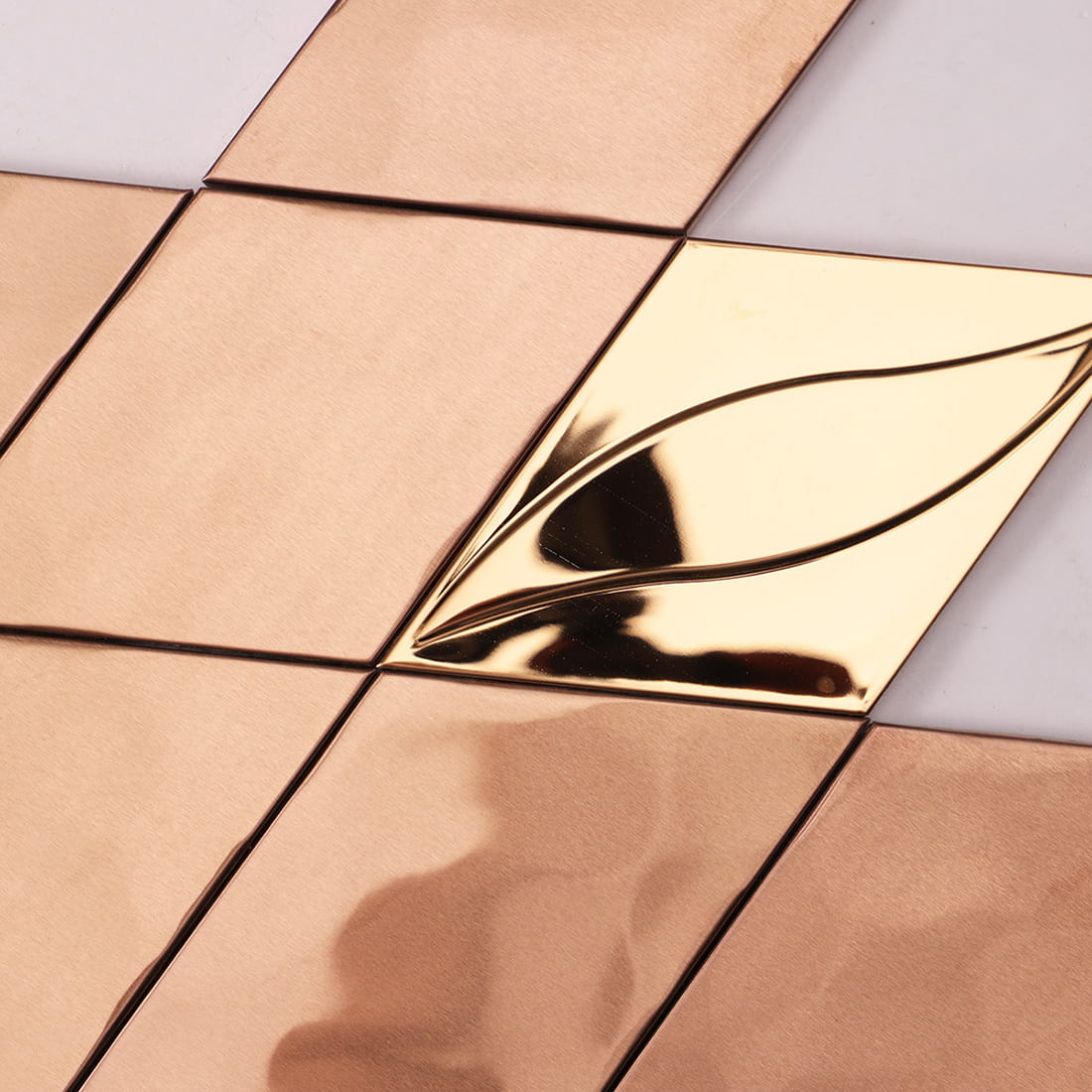 Detail of a rose gold mirror finish metal tile with a 3D leaf design.
