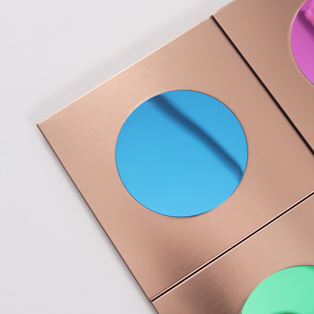Closeup of rose gold square metal tile with reflective blue round glass insert