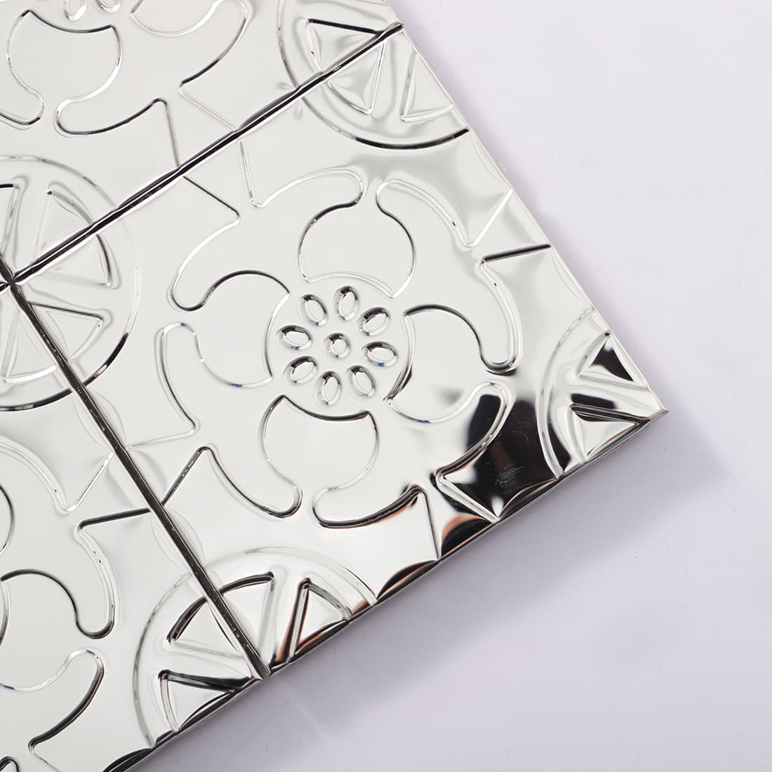 Corner detail of silver stainless steel floral embossed square tiles