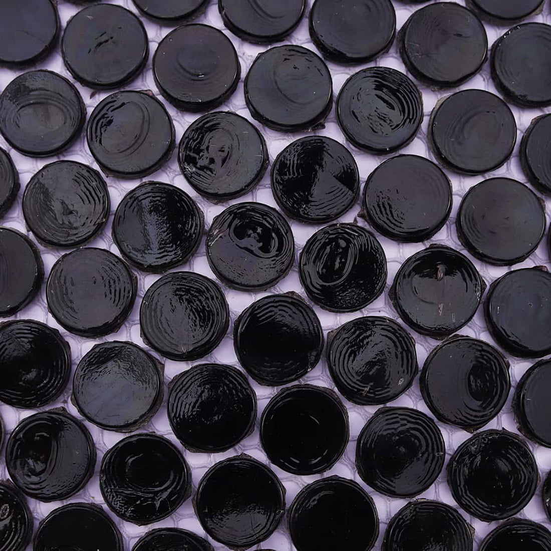 Top-down detail of glossy black round mosaic chips showing natural glass ripples.