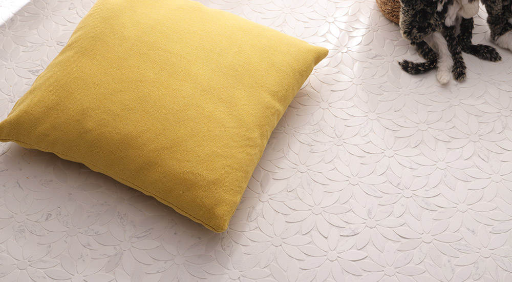 {"default":"Close-up of interlocking daisy pattern white marble mosaic floor tiles with a single yellow pillow."}
