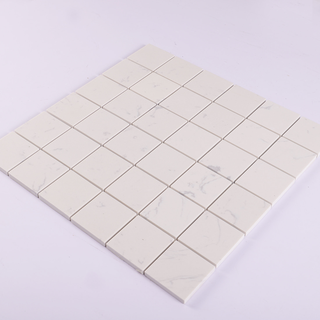 Angled view of white square marble mosaic tile sheet with subtle veining