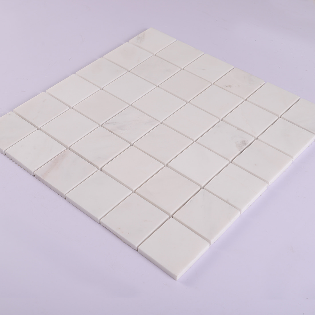 Angled view of white square marble mosaic tile sheet