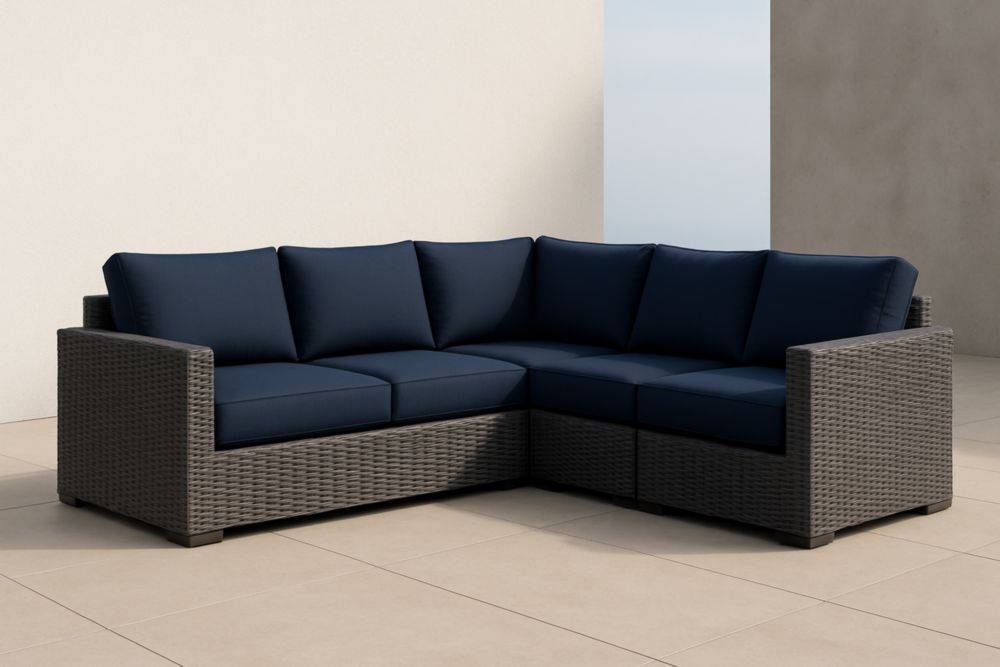 Divano angolare in rattan sintetico grigio con cuscini blu.