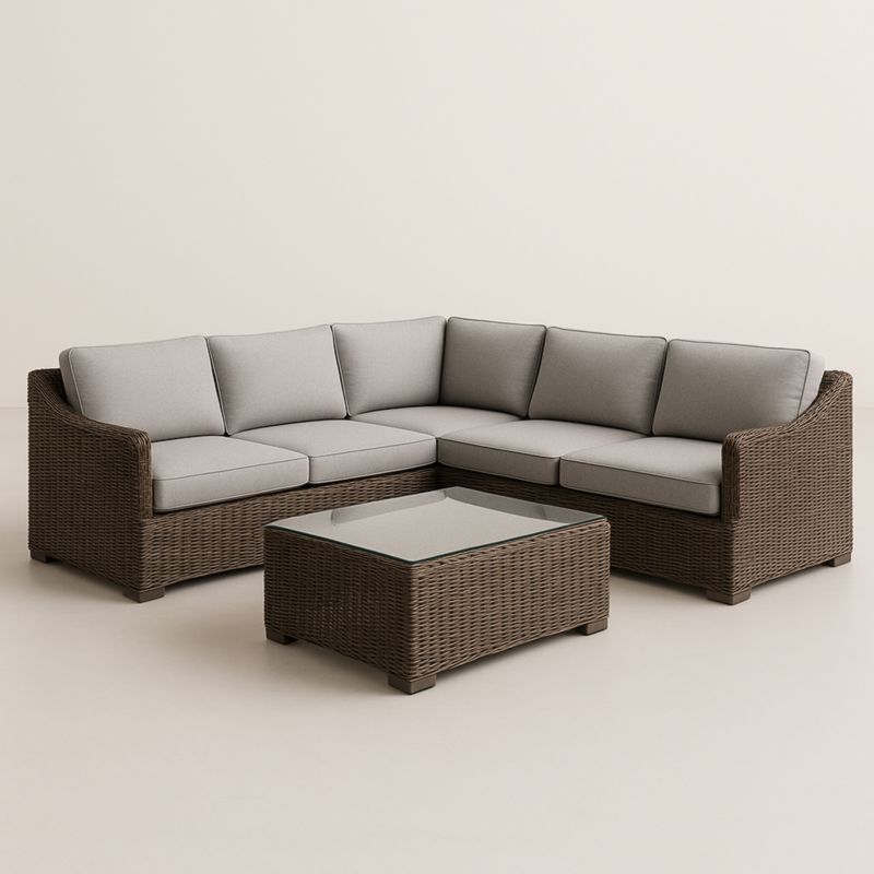 Divano angolare in rattan sintetico con cuscini grigi e tavolino in vetro temperato