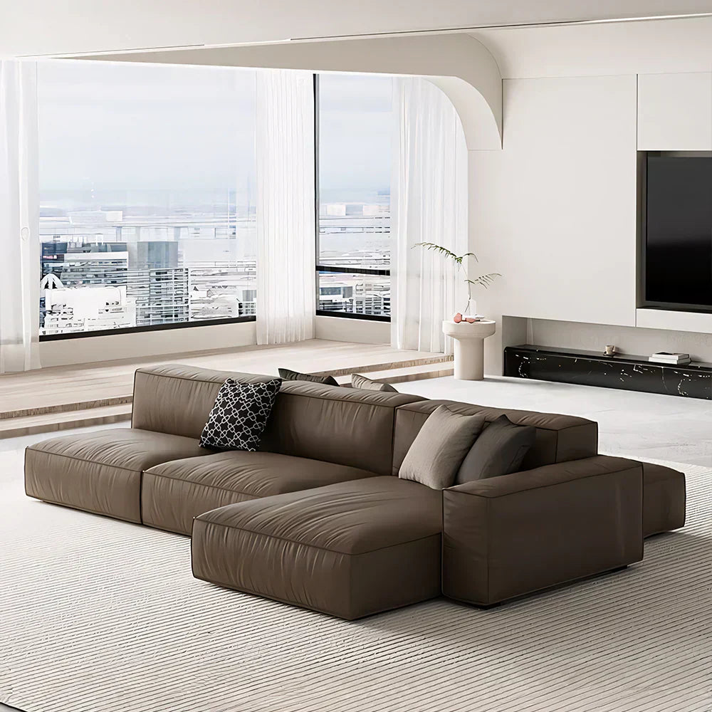 Modern top-grain leather sectional sofa with chaise in a bright minimalist living room with large windows and city view.