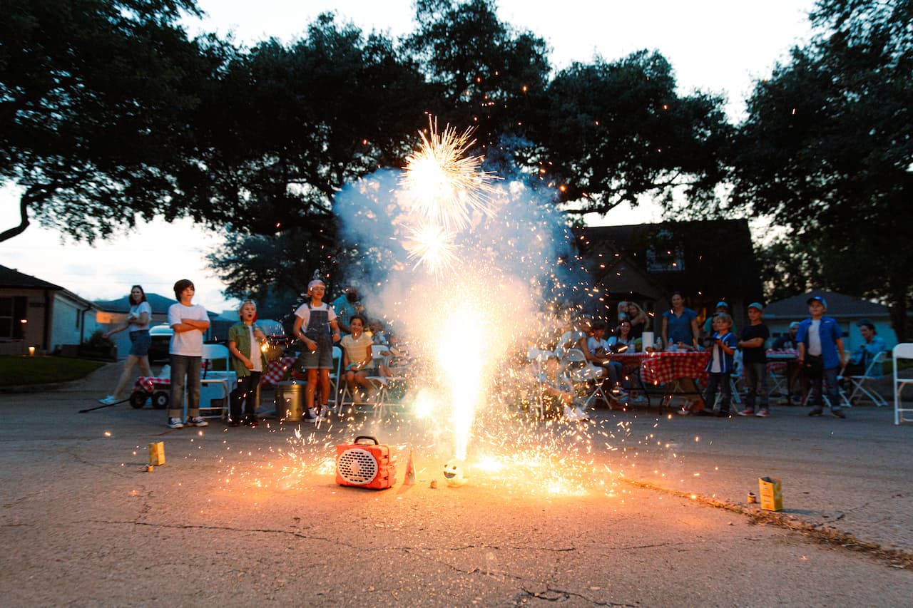 A lifestyle photo from a Original Gen 3 in Orange playing music in a party with fireworks happening close to the speaker.