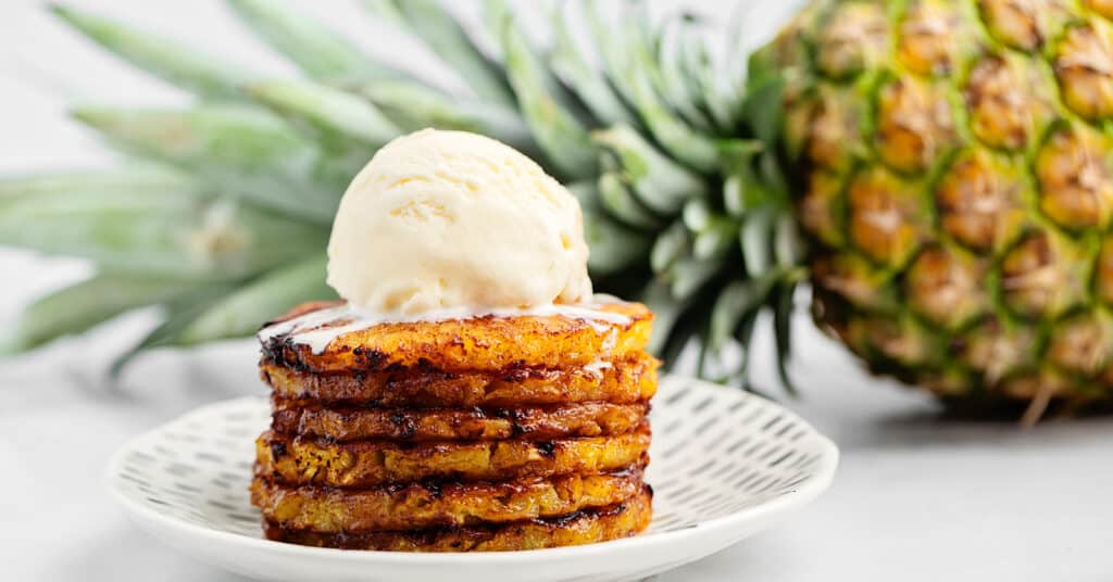 Cinnamon Brown Sugar Air Fried Pineapple Rings Topped with Ice Cream with a Whole Pineapple in the Back