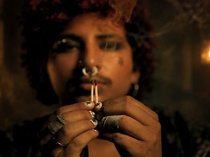 image of man in a moody, candlelit setting showing the sacred sigil press on nail set, which features a parchment colored nail base and black sigil graphics on each nail
