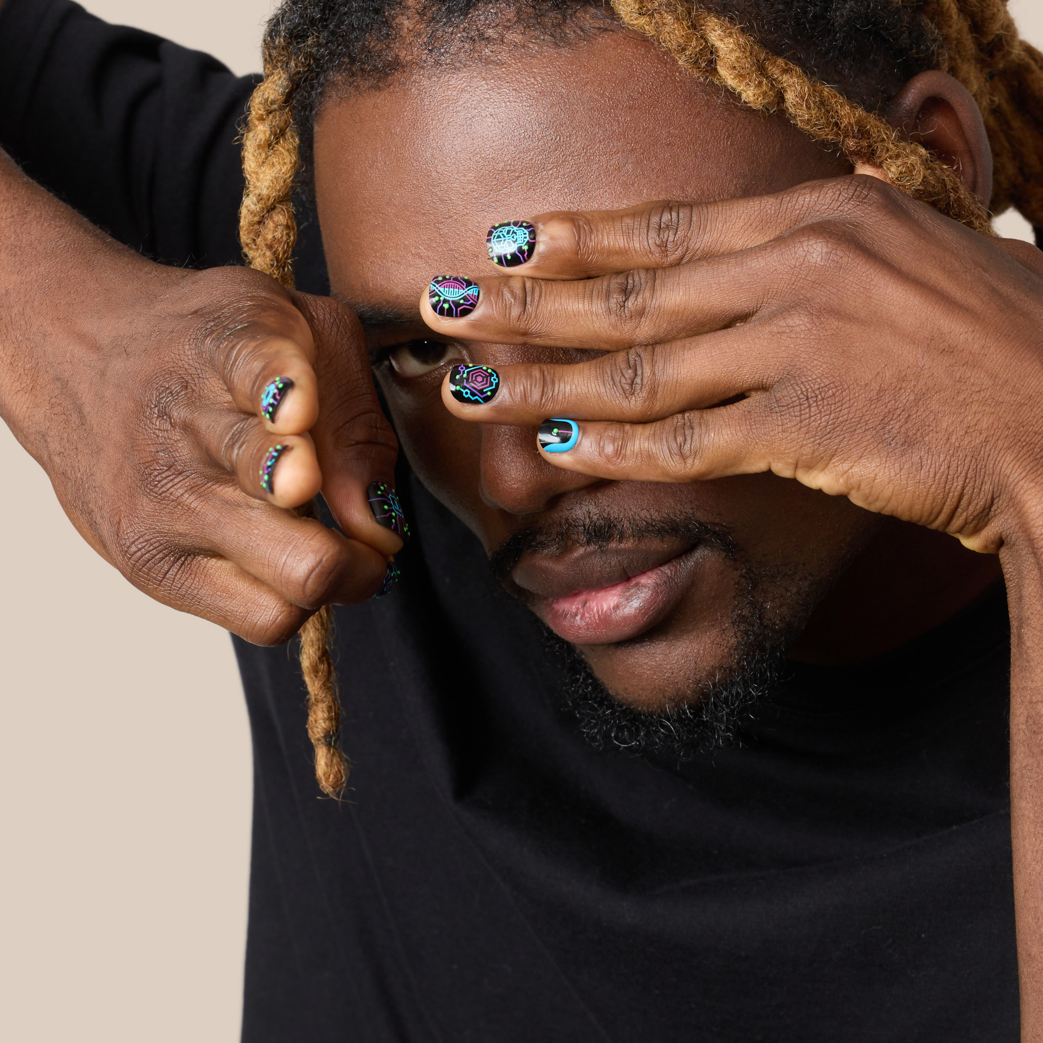 close up image of man wearing the cyber neon press on nail set, which features a glowing circuitry crawling across a matte black base like code breaking through the system. Electric purple and cyan pathways power skull, heart, and eye icons that flicker like glitches in the simulation. 
