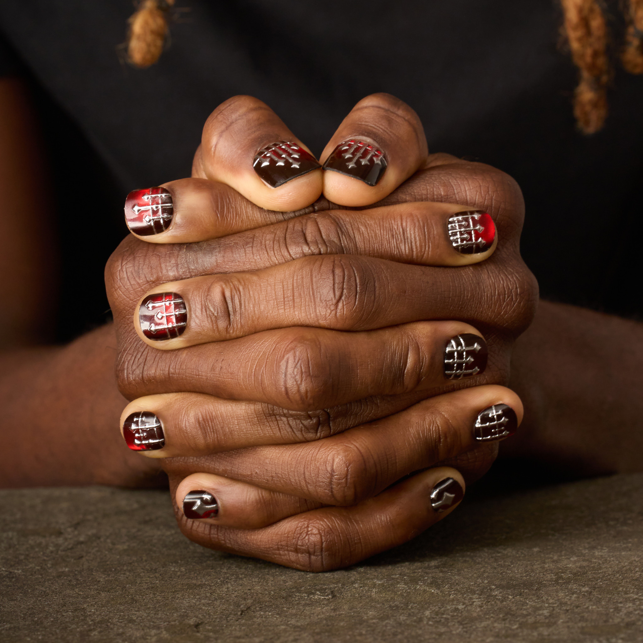 image of man's hands clasped showing press on nails with deep red cateye base and a 3D ornate silver ironwork design