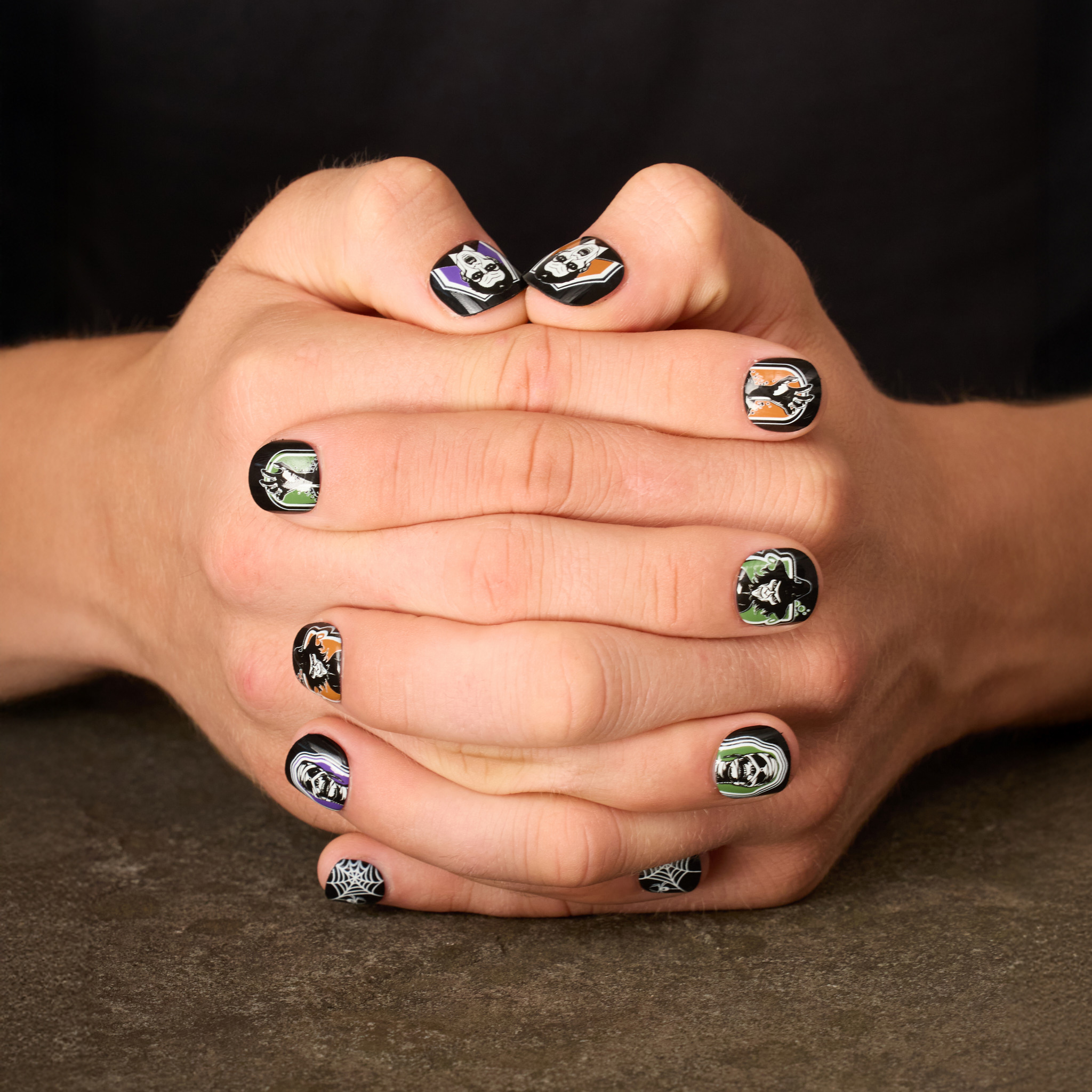 image of man's hands clasped featuring press on nails in classic haunted house designs in a purple, green, and orange palette