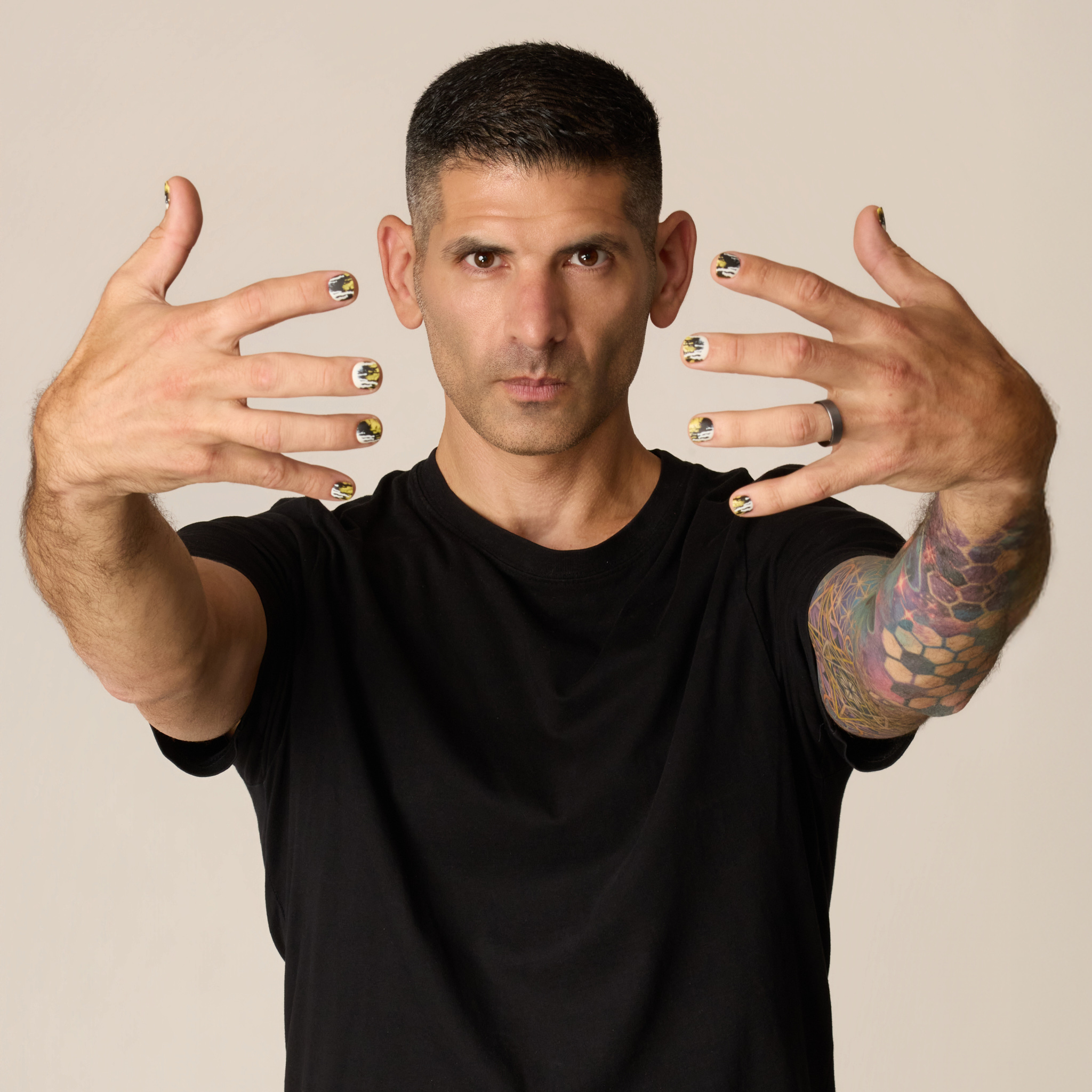 image of man with his hands held in front of his face to showcase the toxic waste press on nail set. this set has a dripped and splattered design in a collision of neon yellow, jet black, and white.