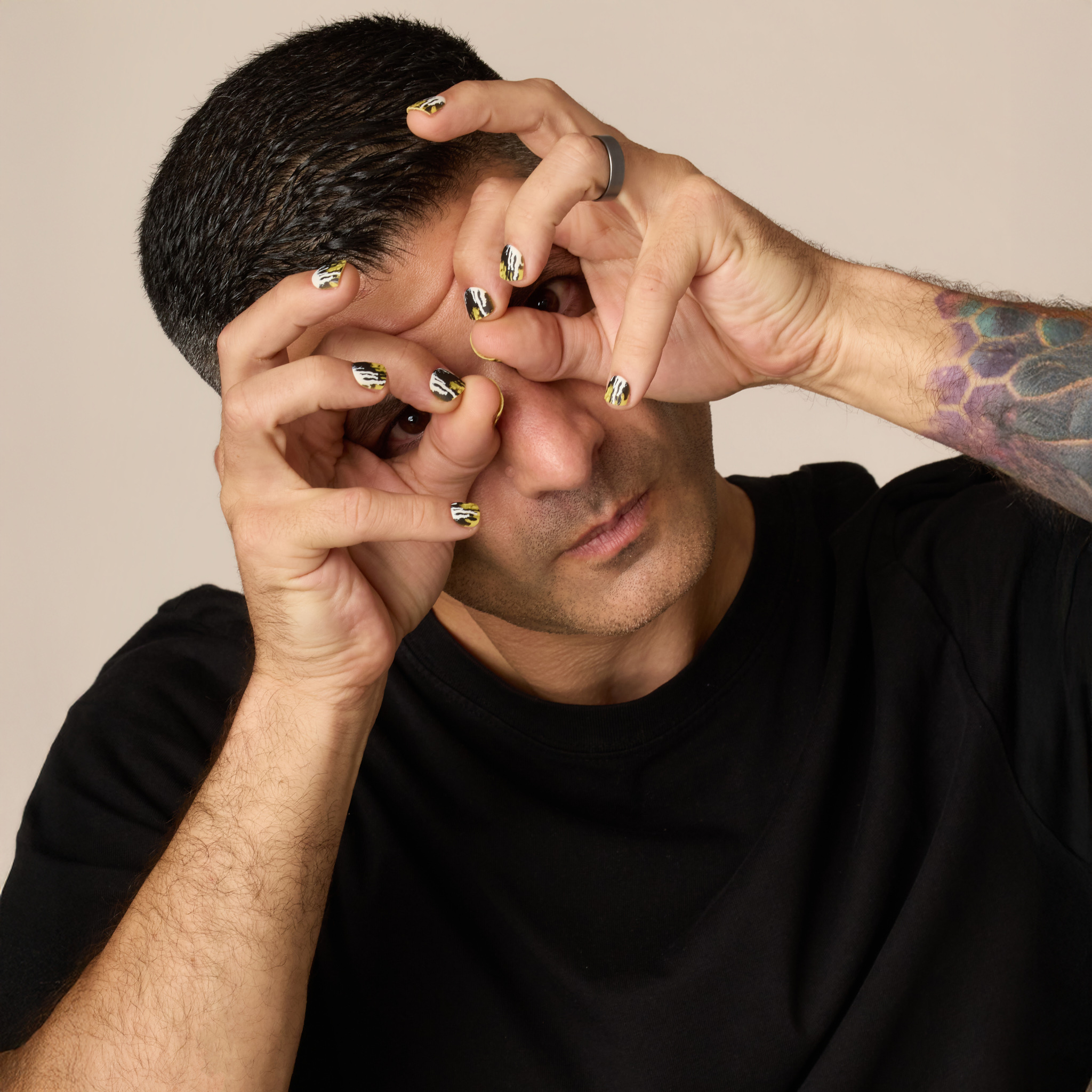 image of man standing with his hands in front of his face to showcase the toxic waste press on nail set. this set has a dripped and splattered design in a collision of neon yellow, jet black, and white.