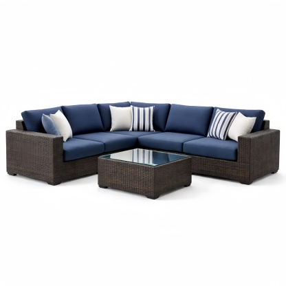 Divano angolare in rattan con cuscini blu e tavolino in vetro temperato