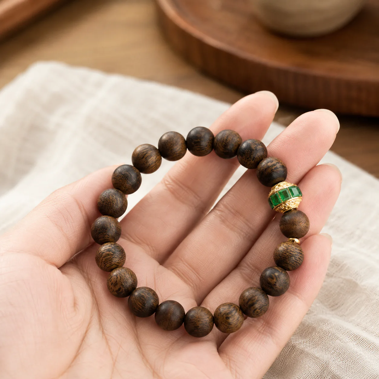 Agarwood bracelet with green gemstone accent held by hand