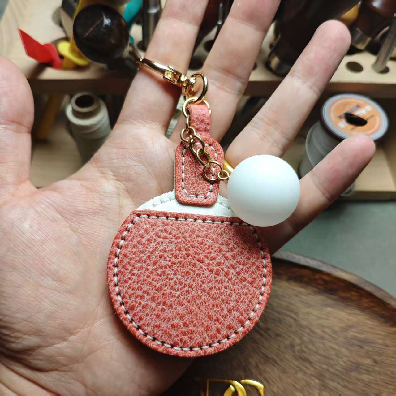 Rose leather charm in hand, real size reference, POP CUIR wooden tray background