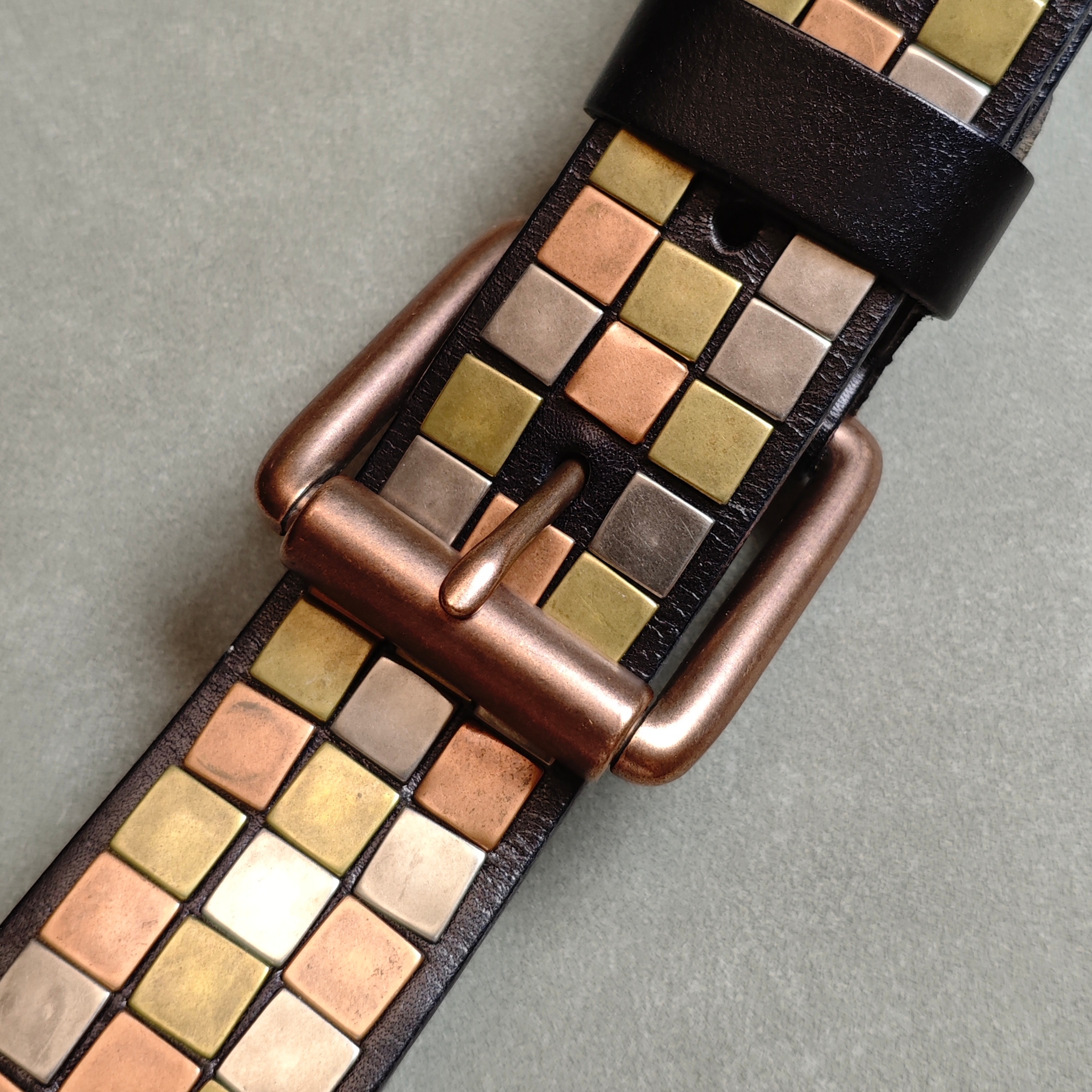 Close-up of black mosaic leather belt showing multi-tone brass copper nickel and rose gold square blocks hand-set in channel