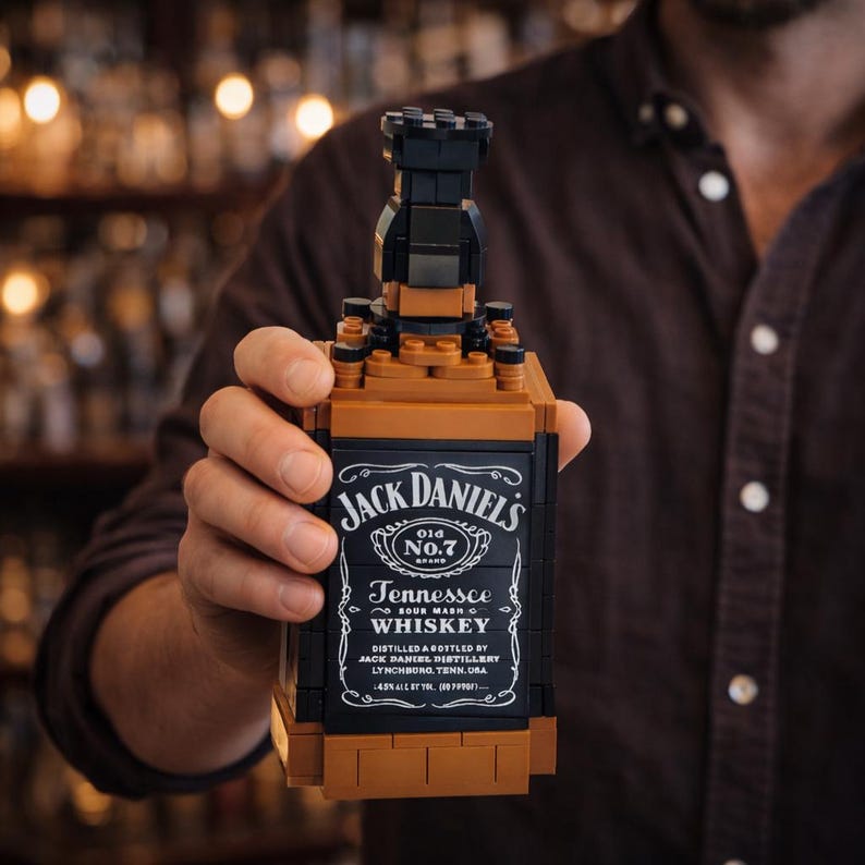 May include: A brown and black brick-built replica of a Jack Daniel's whiskey bottle. The label reads "Jack Daniel's Old No.7 Tennessee Whiskey" with additional text. The bottle is held in a person's hand.