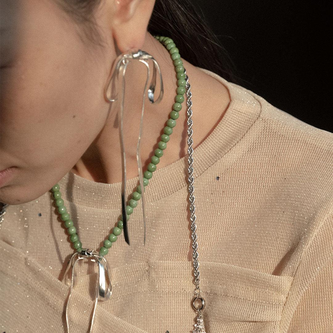 Chloe VINTAGE GREEN BEADED RIBBON NECKLACE featuring a clean chic bow design of Dyed green quartz & Glass beads in small size and vintage green color with gold necklace clasp ,perfect for dailylife/party/office/casual occasion. Displayed in a lifestyle setting with a model wearing a cream top.