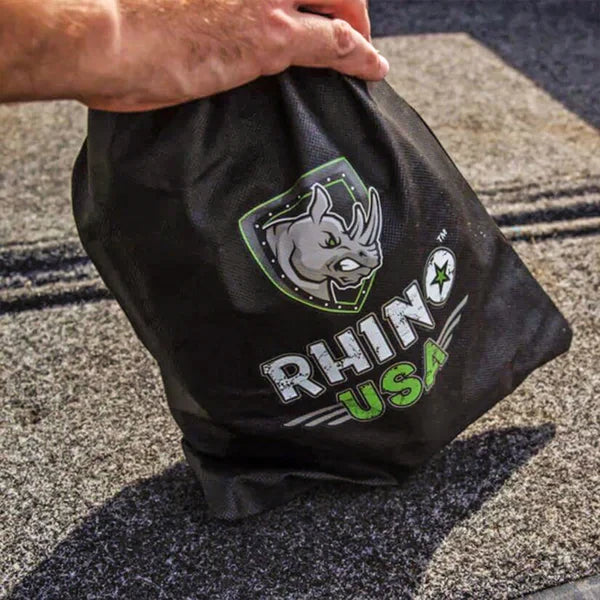 A hand holding a black Rhino USA bag with a logo featuring a rhino head and green accents, placed on a gray textured surface.