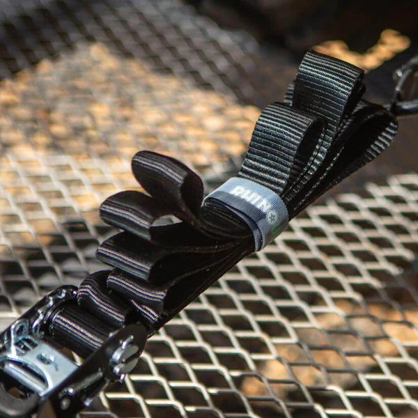 Close-up of a black climbing anchor strap with multiple loops, attached to a metal grid surface. The strap features reinforced stitching and a branded label reading QUINN.