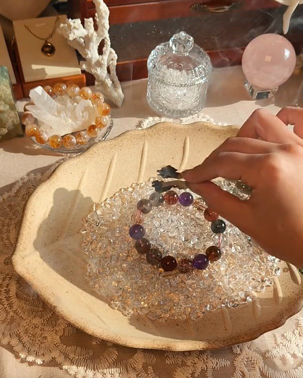 A bracelet resting on clear quartz chips beside a sprig of herbs