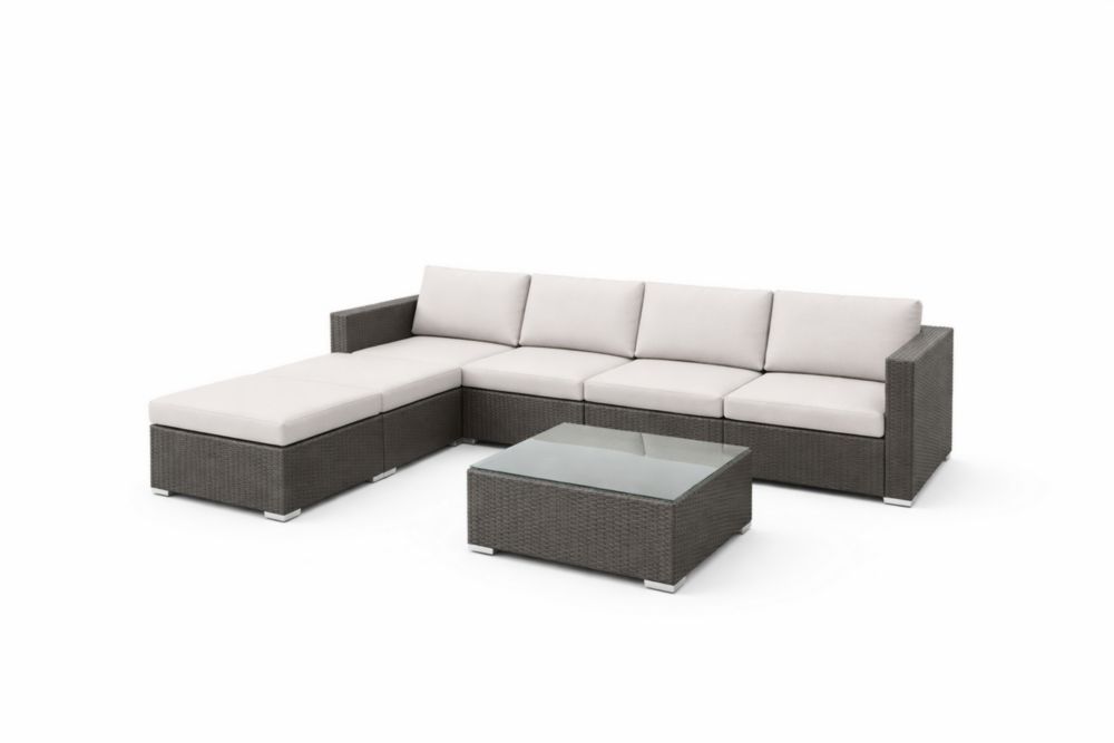 Canapé d'angle extérieur en résine tressée grise avec coussins blancs et table en verre trempé