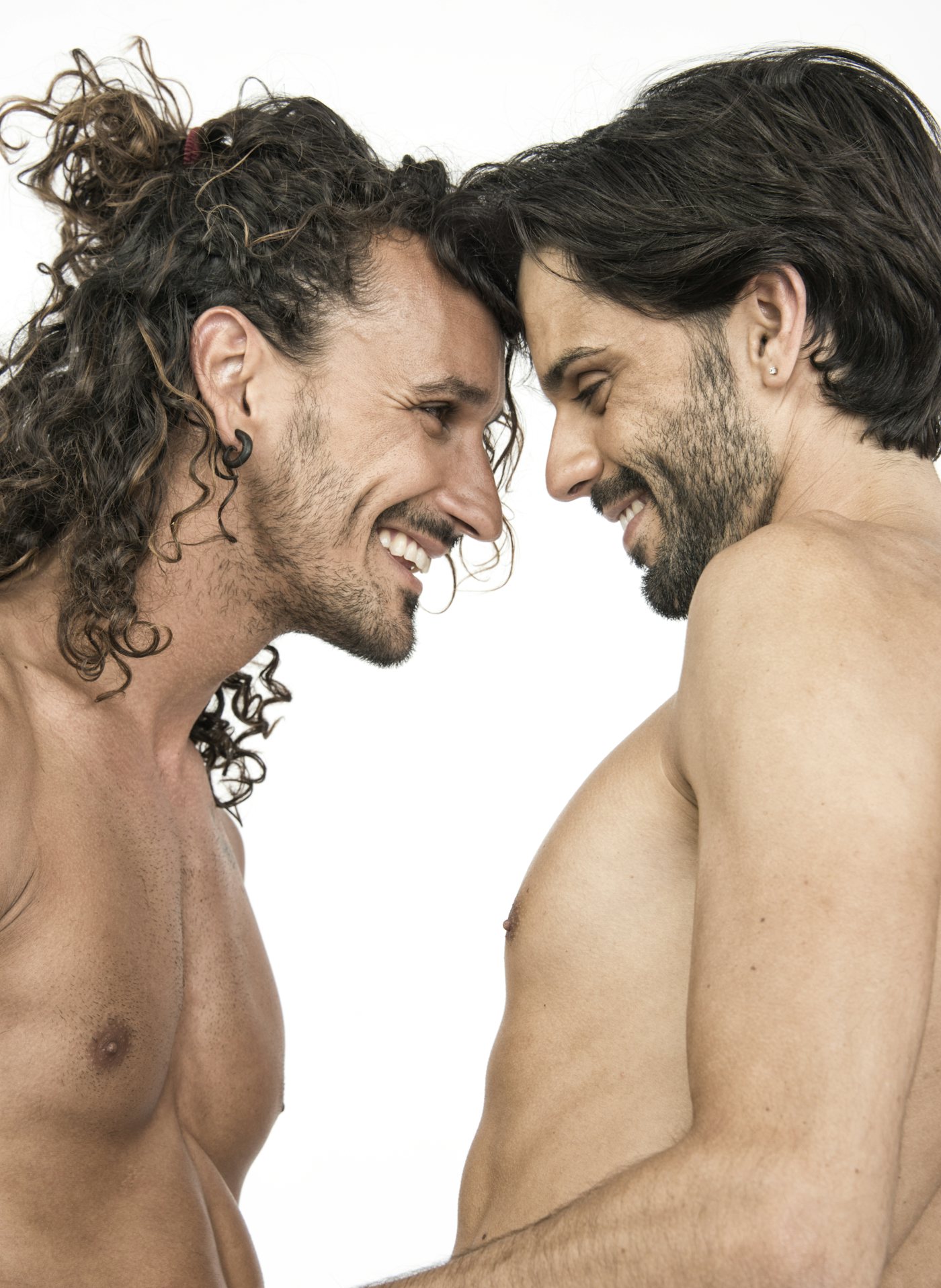 Two shirtless men sharing an intimate moment in a bright studio