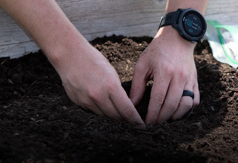 Obr&aacute;zek ukazuj&iacute;c&iacute; ruce osoby s&aacute;zen&iacute; do půdy, kter&aacute; m&aacute; na sobě Garmin chytr&eacute; hodinky