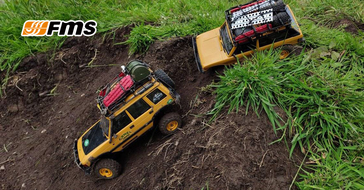 Two yellow FMS mini RC trucks driving through a muddy grass trail
