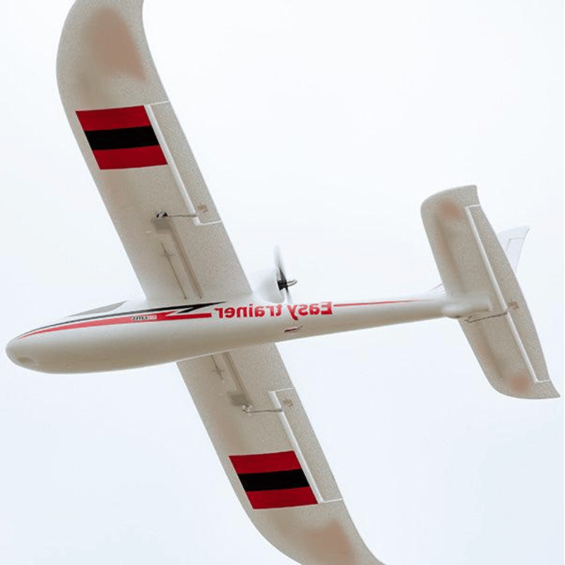 FMS 1280mm Easy Trainer RC plane with red and black wing accents, flying with a clear sky background.