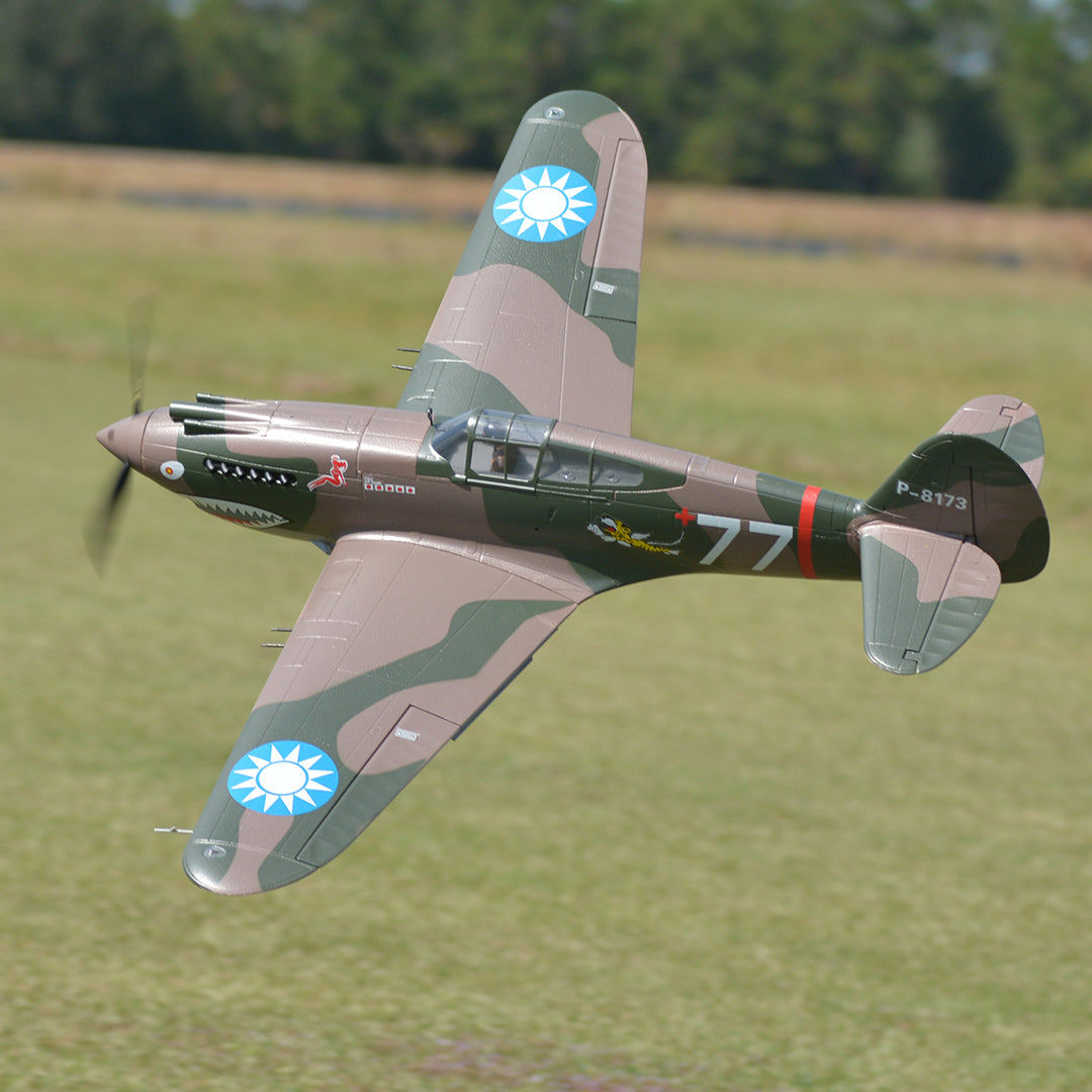 FMS 1400mm P-40B Warhawk Flying Tiger PNP RC plane in flight with camouflage paint, shark teeth nose art, and '77' marking.
