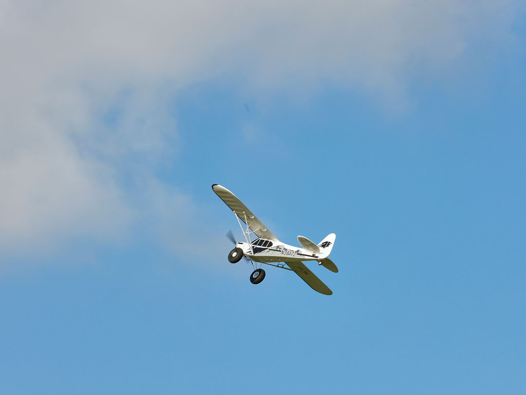 A white RC airplane with a sleek design flying against a blue sky with light clouds.