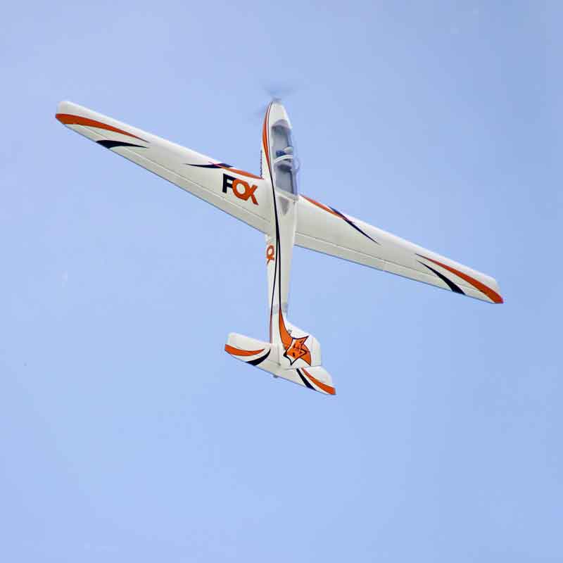 FMS 3000mm Fox aerobatic glider in flight, white with orange and black accents, blue sky.