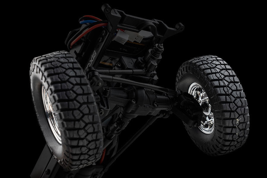 Close-up view of an RC vehicle's suspension system and tires, showcasing intricate details like chrome rims, deep tread patterns, and wiring, set against a dramatic black background.