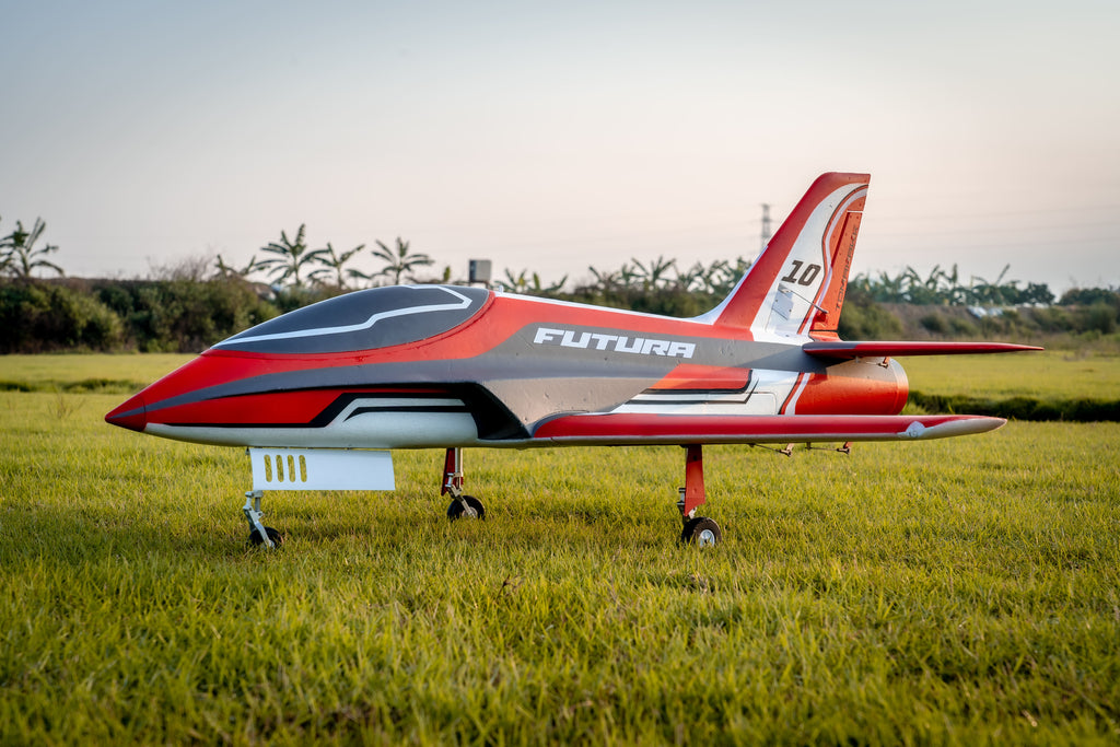 Side profile of the FMS Futura V3 on a grassy field, highlighting its red, gray, and white aerodynamic fuselage