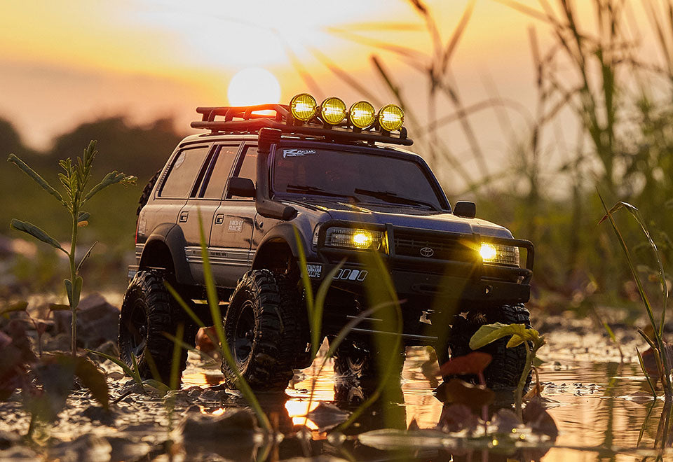 A modified off-road vehicle with lights and accessories, navigating through a scenic outdoor environment at sunset.
