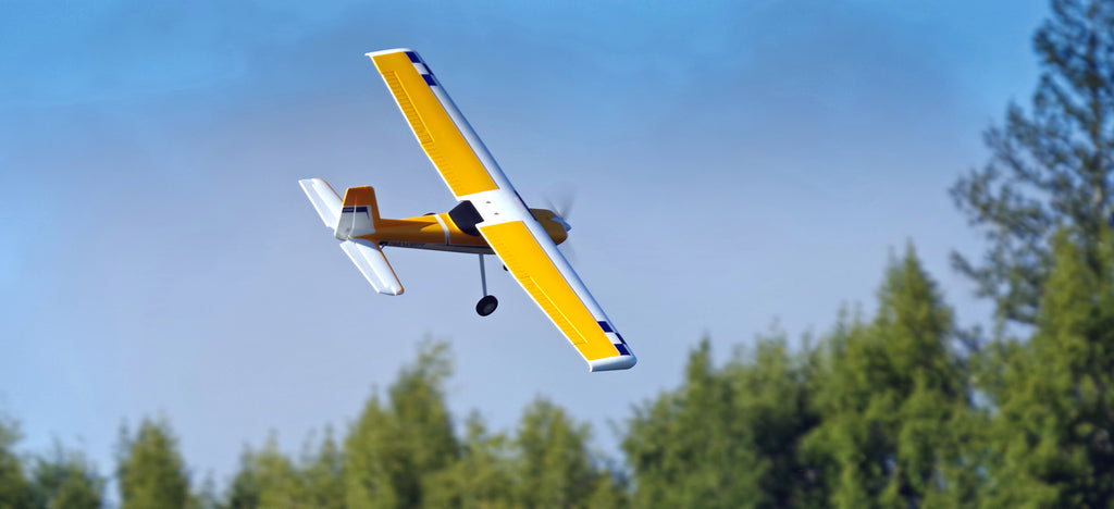 A yellow and white propeller plane flying against a blue sky with a forested landscape below.